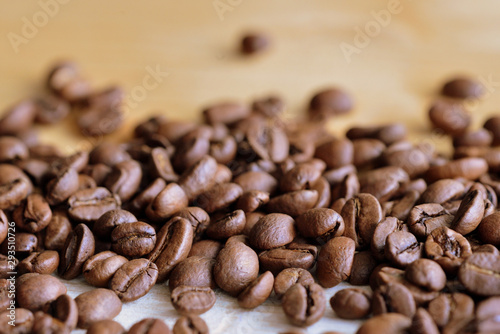 Fototapeta Naklejka Na Ścianę i Meble -  Roasted coffee beans scattered on a wooden surface close up