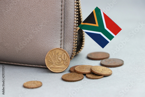 Heap of South African Rand coin money and mini South African flag stick on the leather wallet on grey background.