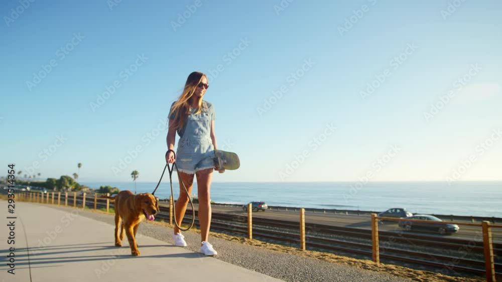 Young happy girl walking golden retriever puppy on beach boardwalk at sunset