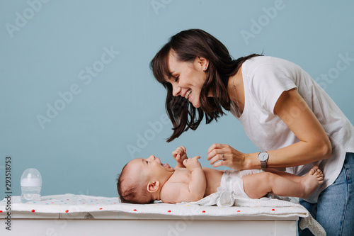 Mother changing diaper on her baby on table over blue background. photo