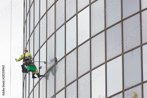 A man worker in worksuit cleaning the exterior windows of a skyscraper - industrial alpinism at overcast weather - hanging on ropes photo