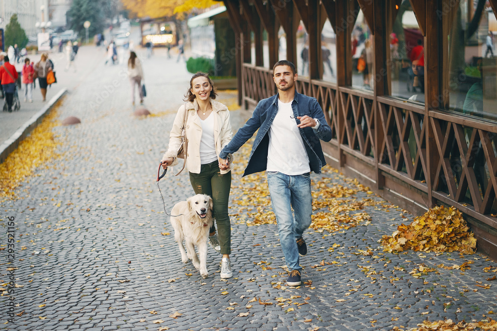 brunette couple walking their golden retriever dog in the city on a sunny autumn day
