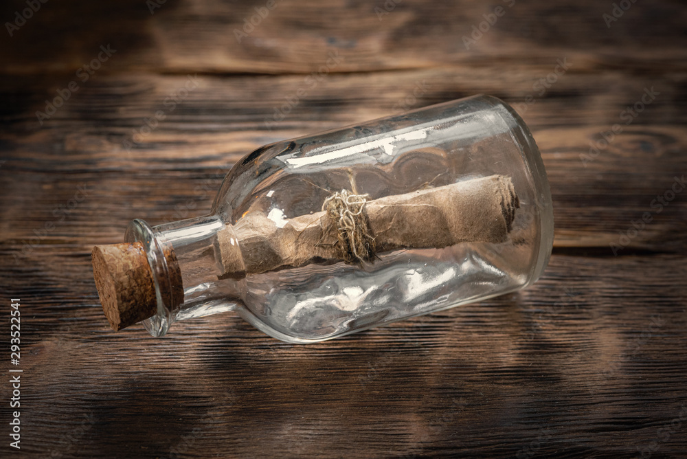 Pirate letter parchment in a glass bottle on brown wooden table background.