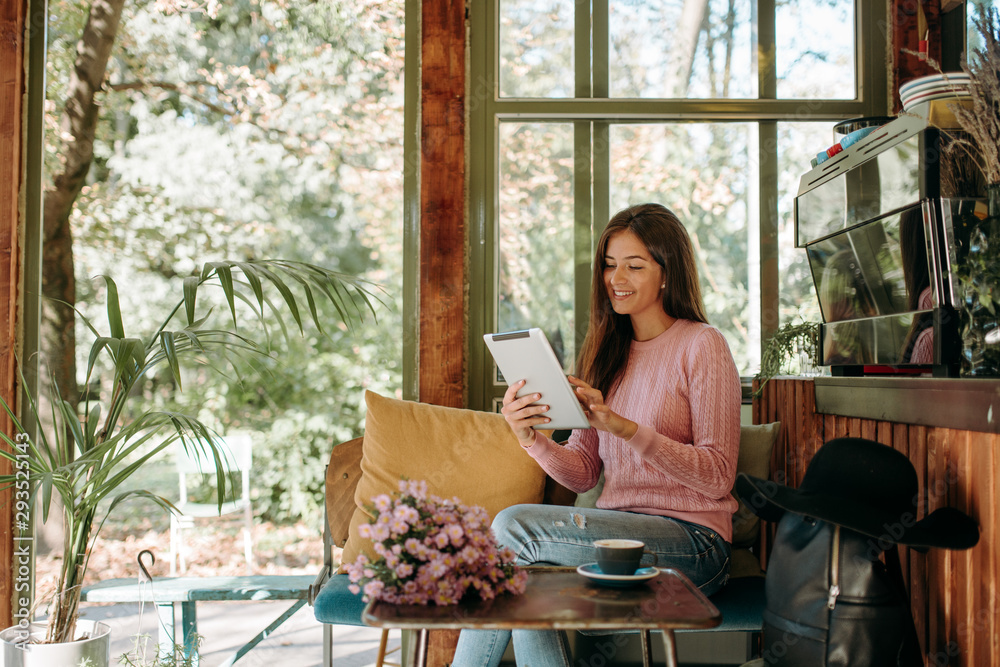 Happy hipster woman in retro cafe. A young girl use a tablet in a cafe while drinking coffee. Happy hipster woman in retro cafe. A young girl use a tablet in a cafe while drinking coffee.