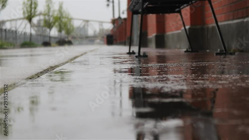 Low shot of ground looking down a rainy boardwalk with background blurred. Along side green trees and benches with rainy reflection on ground. photo