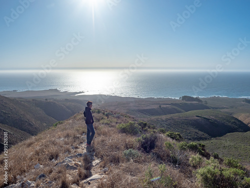 Panorama of boy walking on trail on bluff overlooking sparkling Pacific Ocean on sunny day, sunlight reflecting on ocean, Montana de Oro State Park, Los Osos, California, USA