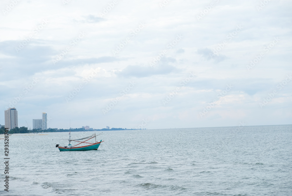 Small Thai fishing green boat in the sea water waving on city  and building background.Commercial fishing boat on the sea ,small fishing trawler flooding on the water with blue clouds sky in Thailand.