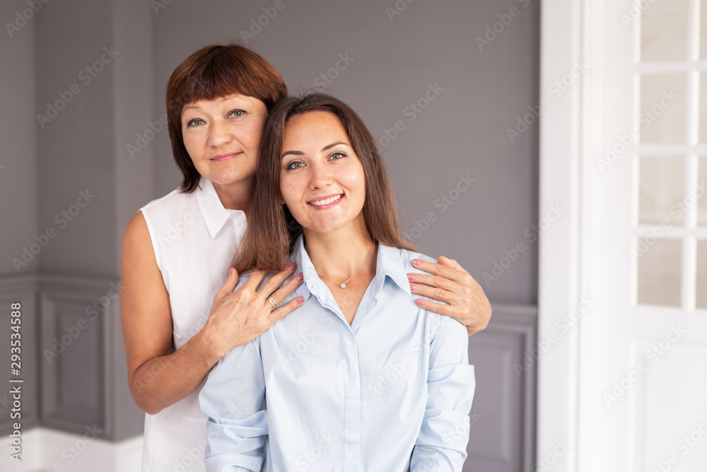 Charming adult woman sits on chair while her mother hugs her. Selective focus Charming adult woman sits on chair while her mother hugs her. Selective focus