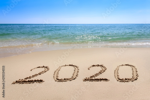 Year 2020 written at the sand beach with sea wave water