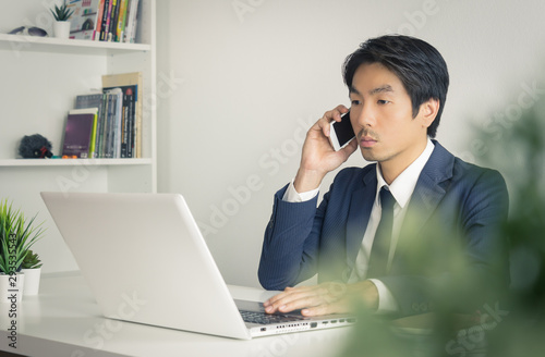 Portrait Asian Businessman in Formal Suit Using Smartphone and Laptop in Office in Vintage Tone