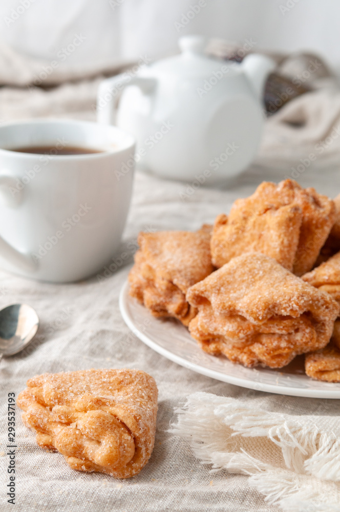 Homemade triangle cookies with curd filling sprinkled with sugar. On a white plate. Background gray linen. In the background is a former teapot and cup. Homemade triangle cookies with curd filling sprinkled with sugar. On a white plate. Background gray linen. In the background is a former teapot and cup.