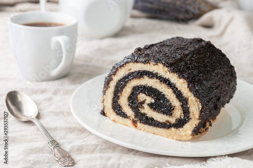 A piece of homemade biscuit roll with poppy seeds. On a white plate. In the background is a white teapot and a mug. Close-up. photo