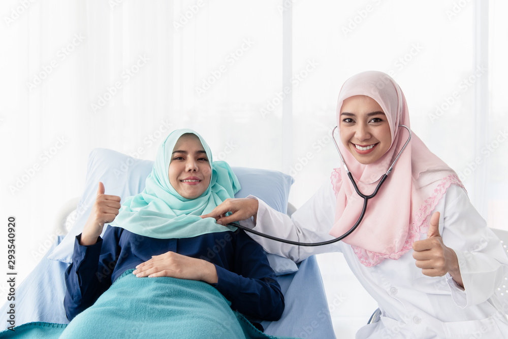 A young beautiful Muslim doctor is using a stethoscope to listen to the patient's heartbeat at the bed in the hospital examination room. A young beautiful Muslim doctor is using a stethoscope to listen to the patient's heartbeat at the bed in the hospital examination room.