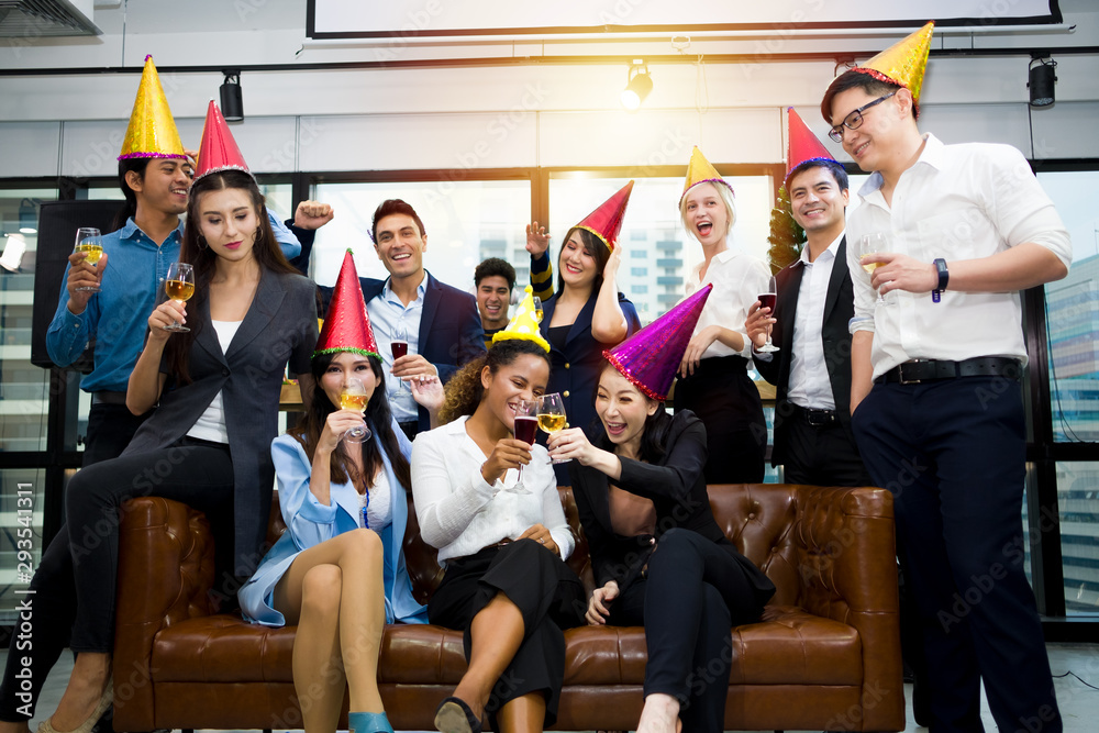 Group of happy colleagues having fun at a new year celebration ahead or business success. Coworkers with diverse ethnicities are toasting wine or champagne glasses at the office party.