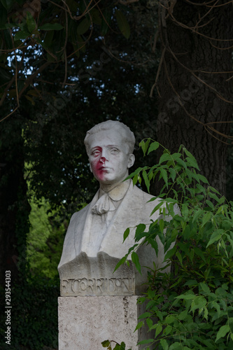 A damaged by vandals concrete bust of R. Corridoni with red paint on the face looking like blood in the park at Villa Borghese