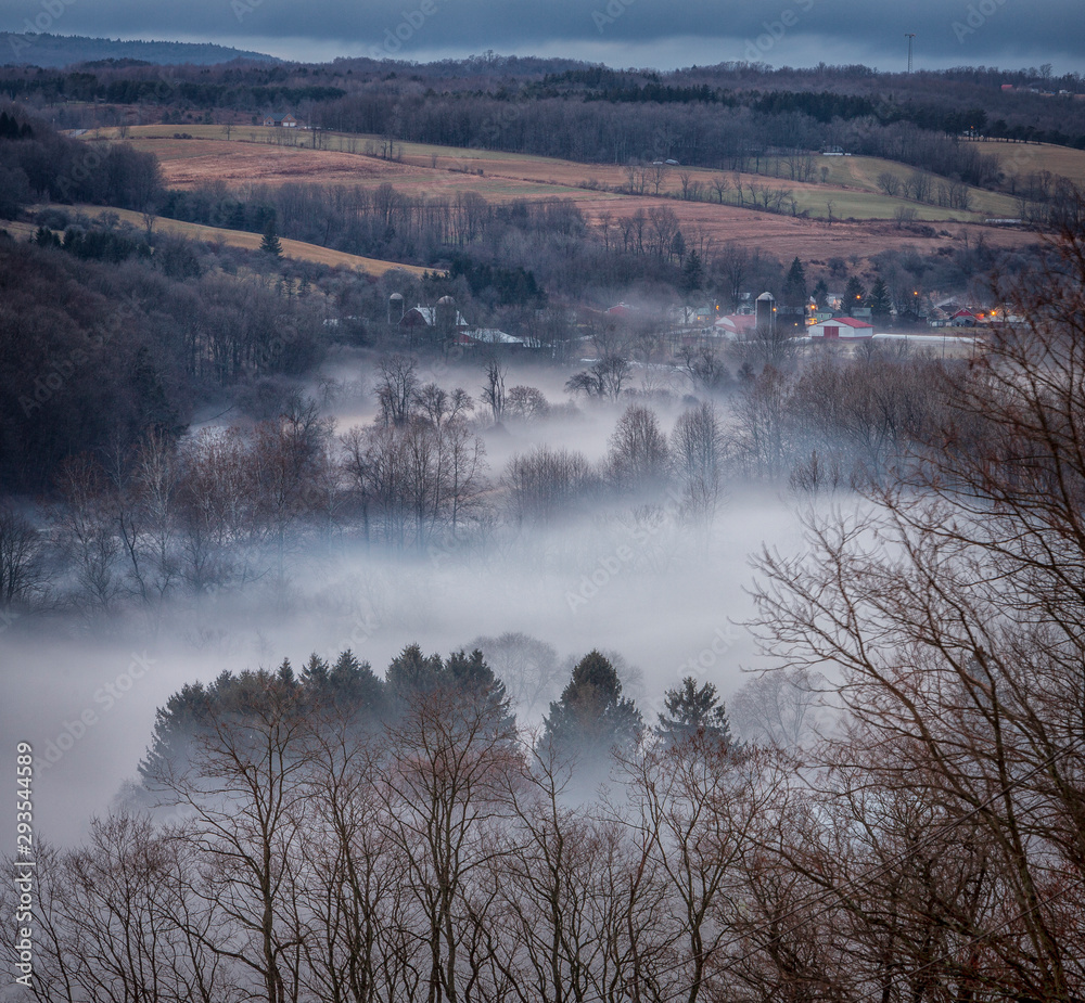 A warm winters fog haunts a New York State landscape of rolling hills of farmland.