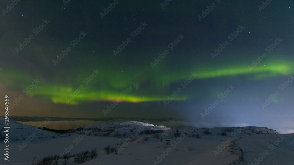 Northern lights, aurora in the sky at night. Hills and rocks covered with snow.