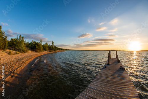 Fototapeta Naklejka Na Ścianę i Meble -  Orange summer sunset at a lake behind a jetty