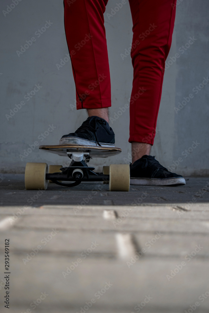 Male adult skateboarder wearing red pants and black sneakers standing with one foot on skateboard ground level view Male adult skateboarder wearing red pants and black sneakers standing with one foot on skateboard ground level view