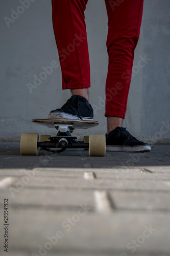Male adult skateboarder wearing red pants and black sneakers standing with one foot on skateboard ground level view