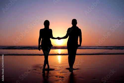  Silhouette of a young couple in love who holds hands on the beach at sunset