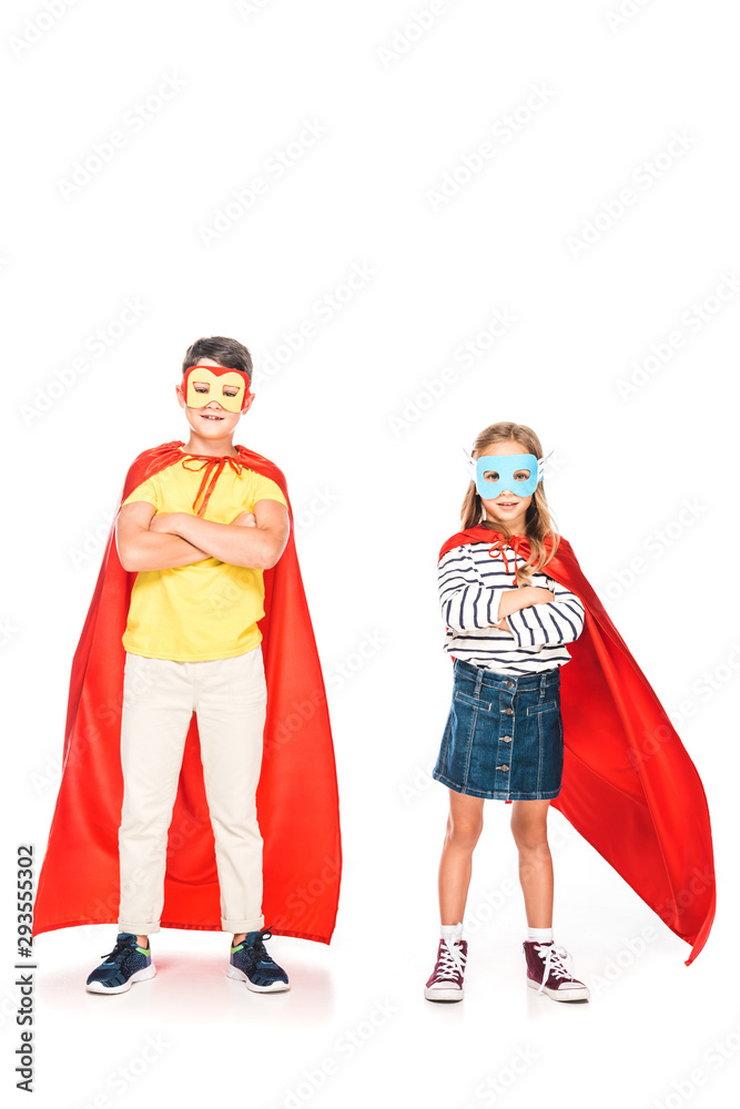 full length view of two kids in hero cloaks standing with crossed arms on white