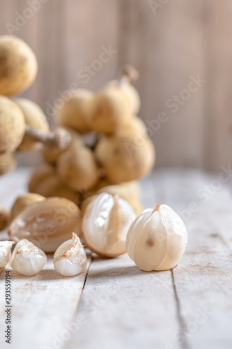 Mix of peeled and clusters whole of exotic Thai fruit called Longkong or lansium parasiticumor southern langsat on wooden table and background. It is a famous sweet tropical fruit in southeast asia.