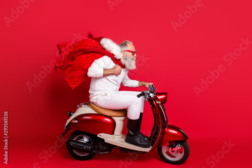 Profile side view of nice bearded gray-haired Saint Nicholas riding motor delivering carrying desirable purchase things December wintertime isolated on bright vivid shine red background