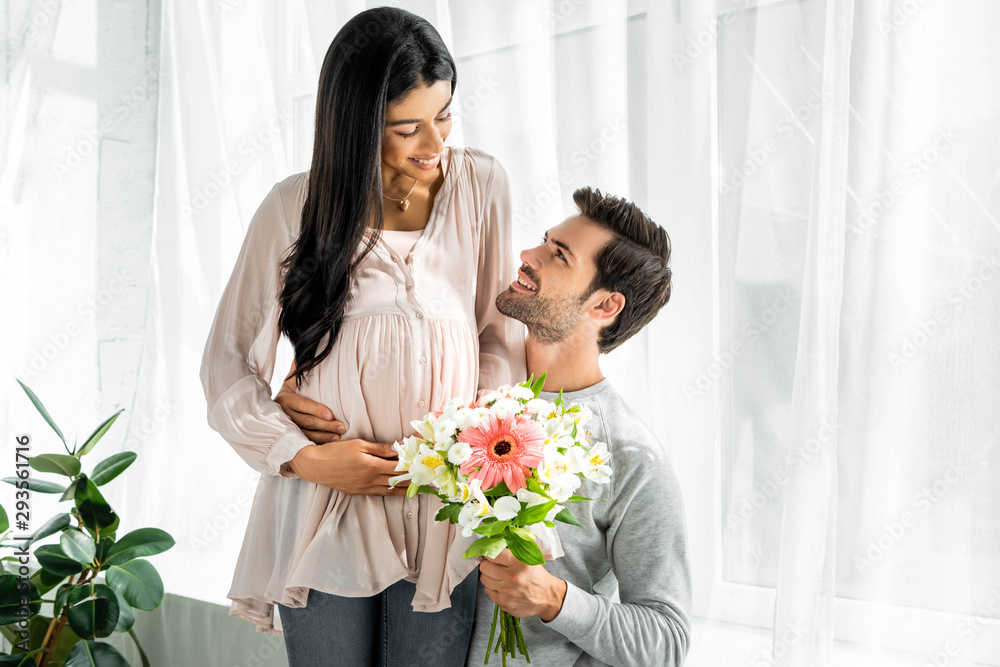 handsome man hugging belly of his pregnant african american woman and holding bouquet handsome man hugging belly of his pregnant african american woman and holding bouquet