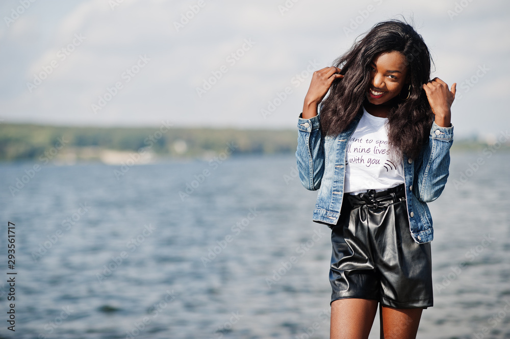 African american dark skinned slim model posed in a black shorts and jeans jacket against sea side. African american dark skinned slim model posed in a black shorts and jeans jacket against sea side.
