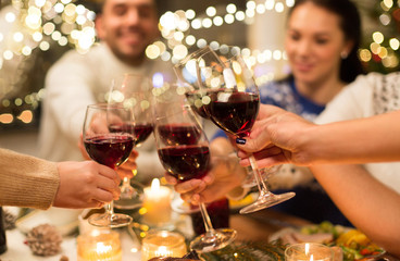 holidays and celebration concept - close up of happy friends having christmas dinner at home, drinking red wine and clinking glasses