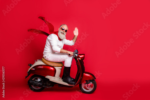 Aged santa man with grey hair move party by vintage moped wear white jumper and trousers isolated red background