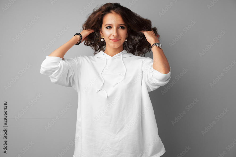 Young brunette woman touching her long shiny hair over gray background Young brunette woman touching her long shiny hair over gray background
