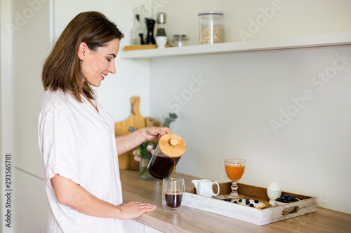 breakfast concept - woman in pajamas pouring coffee from french press