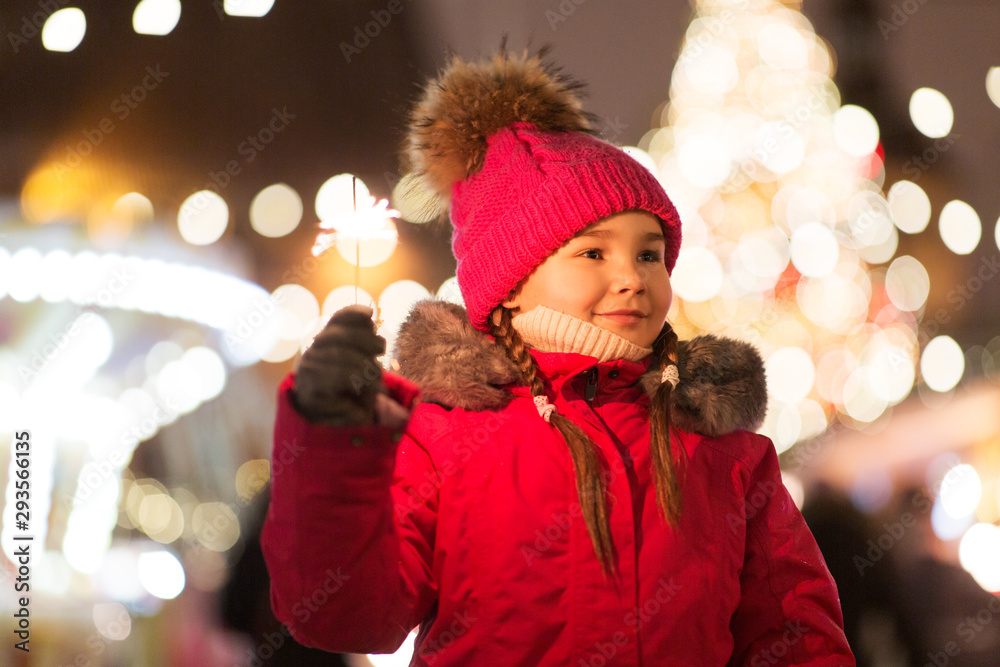 holidays, childhood and people concept - happy little girl with sparkler at christmas market in winter evening