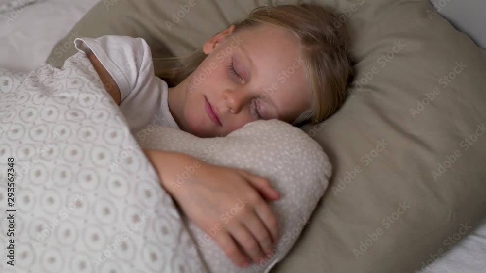 Close-up portrait of cute blonde baby sleeping sweetly in her crib hugging a pillow, sliding camera