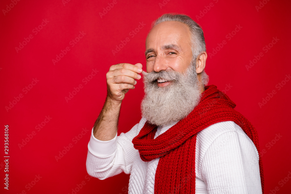 Close up photo of attractive pensioner looking touching his mustache wearing white pullover isolated over red background