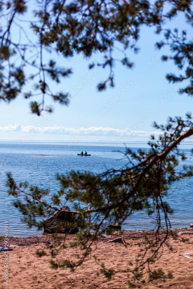 Obraz premium Ocean kayaking near coast. Kajak fahren auf offenem Meer nahe der Küste. Blick durch Bäume auf Kajakfahrer.