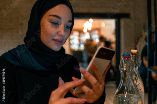 Muslim woman in cafe shopping online using modern mobile phone. Concept of living full life with contemporary modern attitude from tolerable society. Active lifestyle of muslim woman.