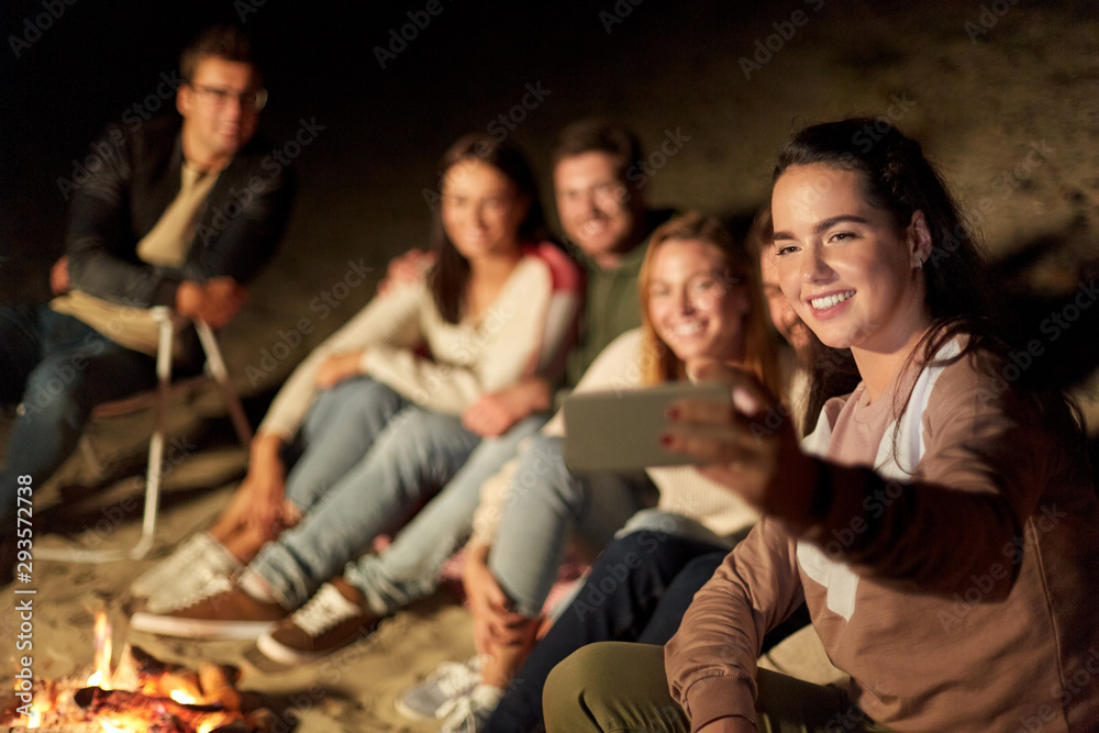 leisure and people concept - group of smiling friends sitting at camp fire taking selfie by smartphone on beach at night leisure and people concept - group of smiling friends sitting at camp fire taking selfie by smartphone on beach at night
