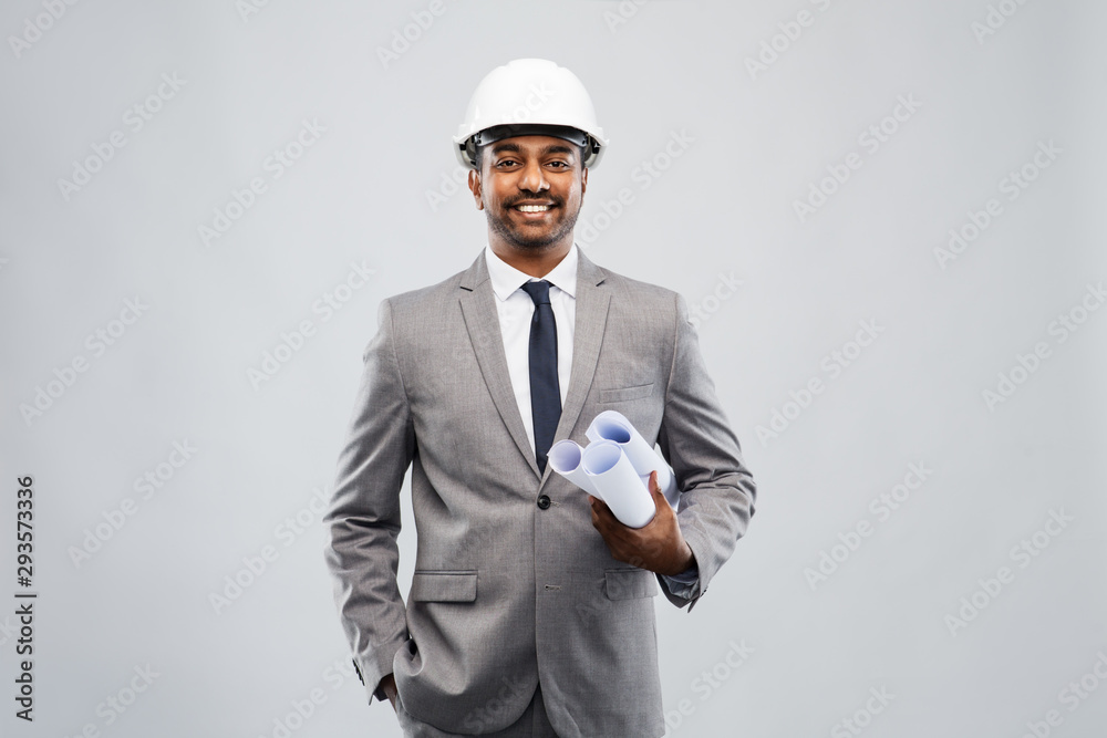 architecture, construction business and people concept - smiling indian male architect in helmet with blueprints over grey background architecture, construction business and people concept - smiling indian male architect in helmet with blueprints over grey background