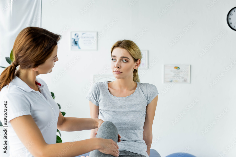chiropractor touching leg of attractive patient in grey t-shirt
