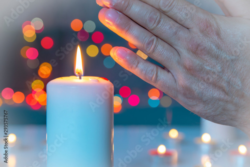 Folded hands for prayer or meditation by a lighted candle. Burning candle symbol of eternity and remembrance of the dead. Religious tradition. All Saints' Day. Bokeh background. photo