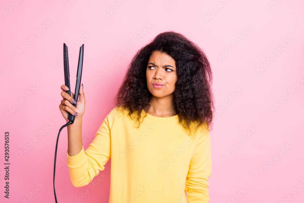 Obraz premium Portrait of minded pensive afro american girl hold look hair straightener think will it be good feel unsure wear yellow clothes isolated over pink color background