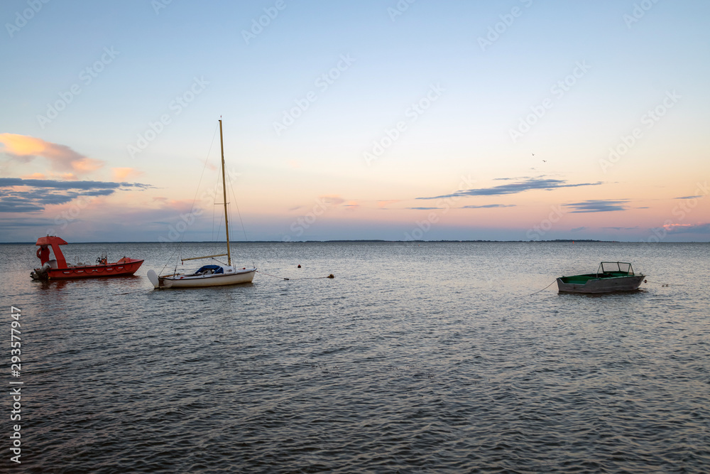 Fishing boats docked at the pier by the shore at sunset. Yachts on the water with colourful sunset sky in the background