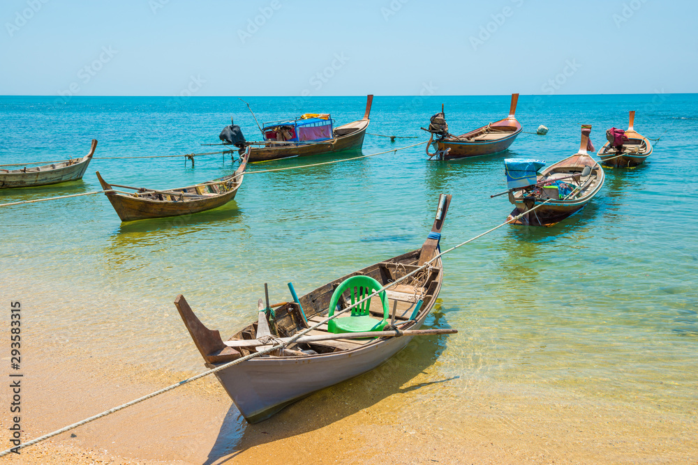 Rows of many traditional wooden fishing long tail boats moored at tropical sand beach with rocks