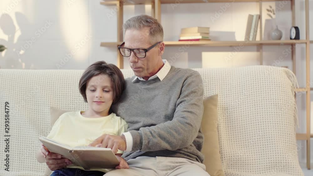 grandpa and grandson reading book together in living room grandpa and grandson reading book together in living room