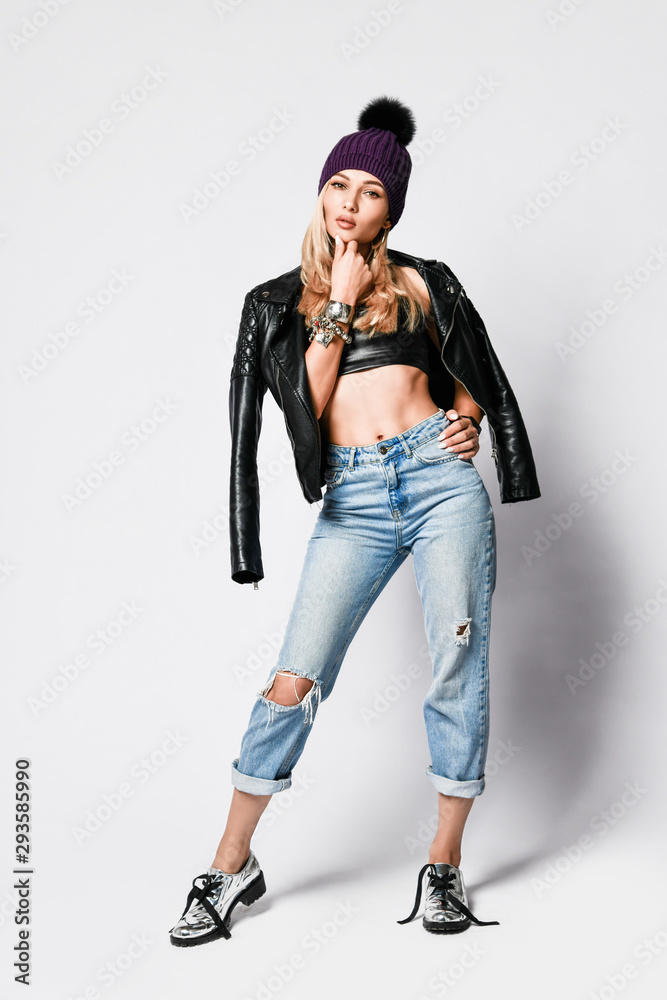 Glamorous brutal style girl in torn jeans, leather top, leather jacket and brutal silver boots is standing thinking