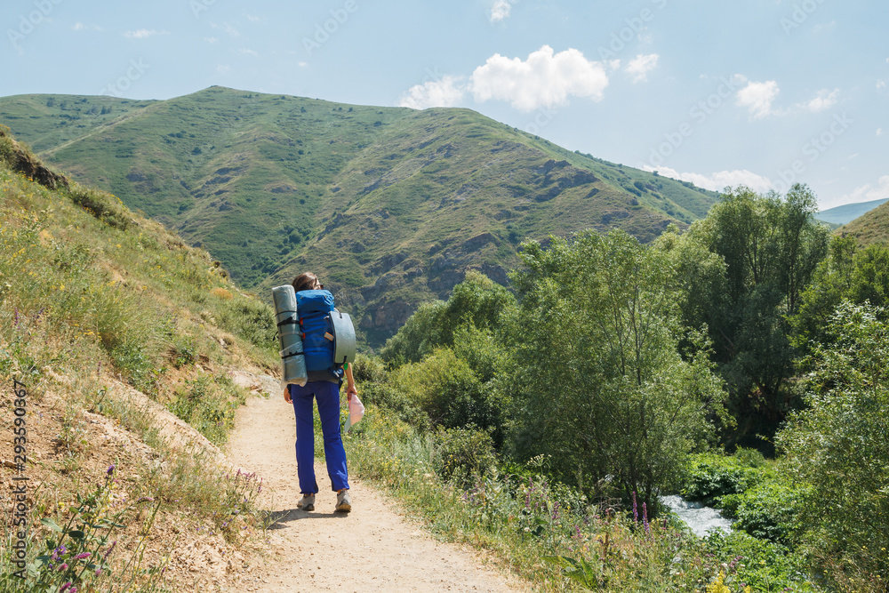 Traveling woman with backpack walking in mountainous area. Female traveler dressed in camping equipment walking along path.