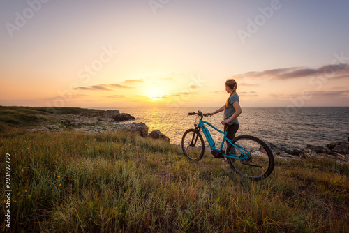 Woman with a bike in the nature   Morning view of a woman with a bike enjoys the view of sunrise at the rocky Black Sea coast